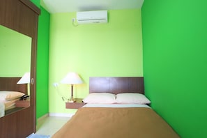 Een kamer met een bed, een nachtkastje met lamp, een wandairconditioner en een spiegel.