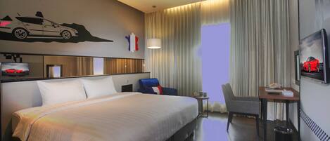 A hotel room with a large bed, a desk with a chair, a TV, and a wall with a car image.