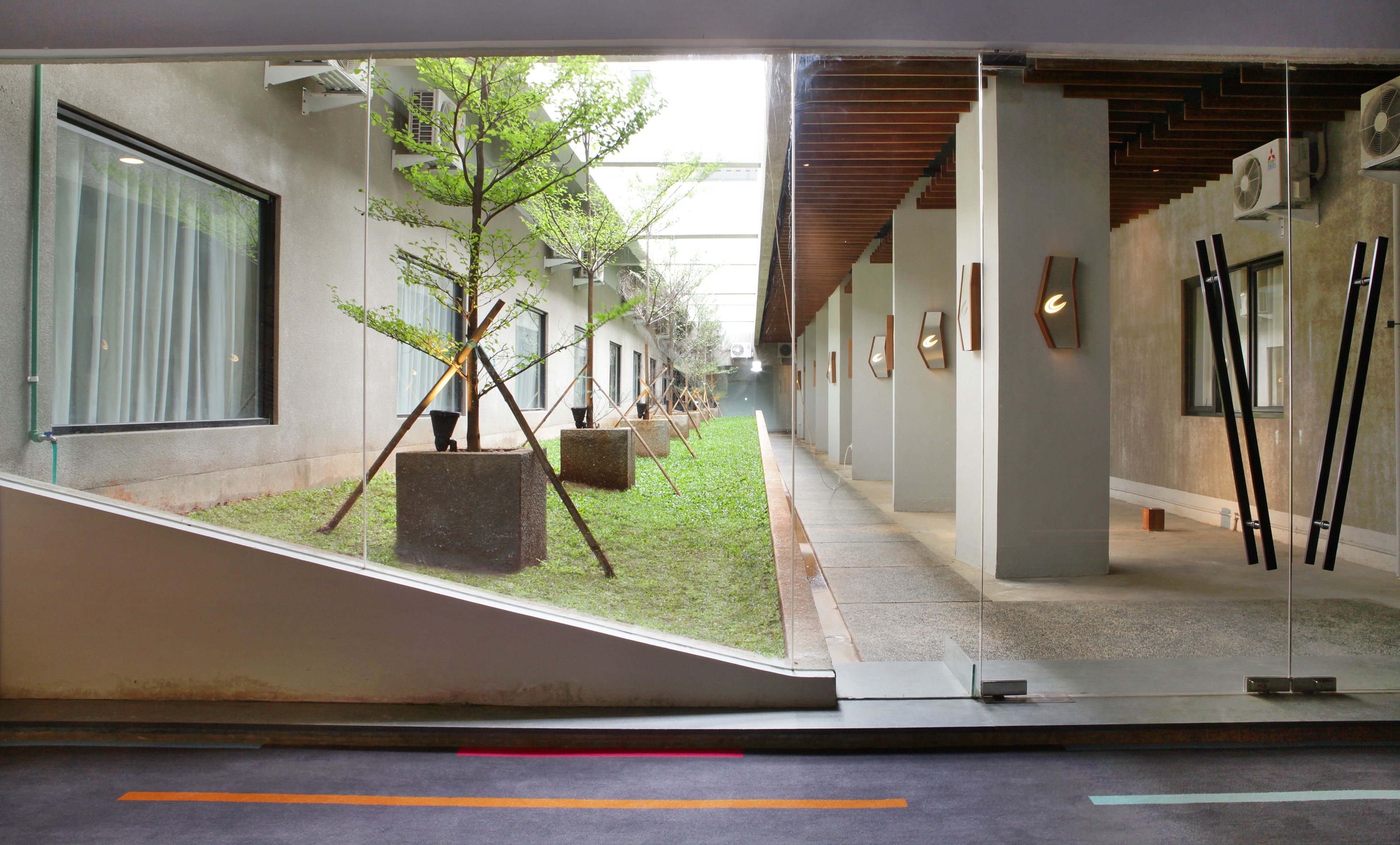 A modern building with a glass facade, a small courtyard with a tree, and a staircase leading to an upper level.