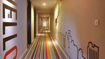 A hallway with a striped carpet, a 'HELLO' sign on the left, and a cityscape mural on the right.