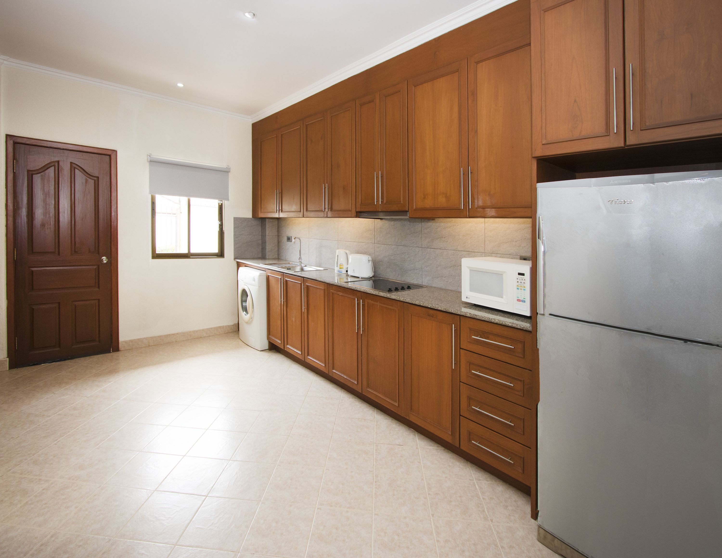 Cozinha com armários de madeira, máquina de lavar, micro-ondas e geladeira.
