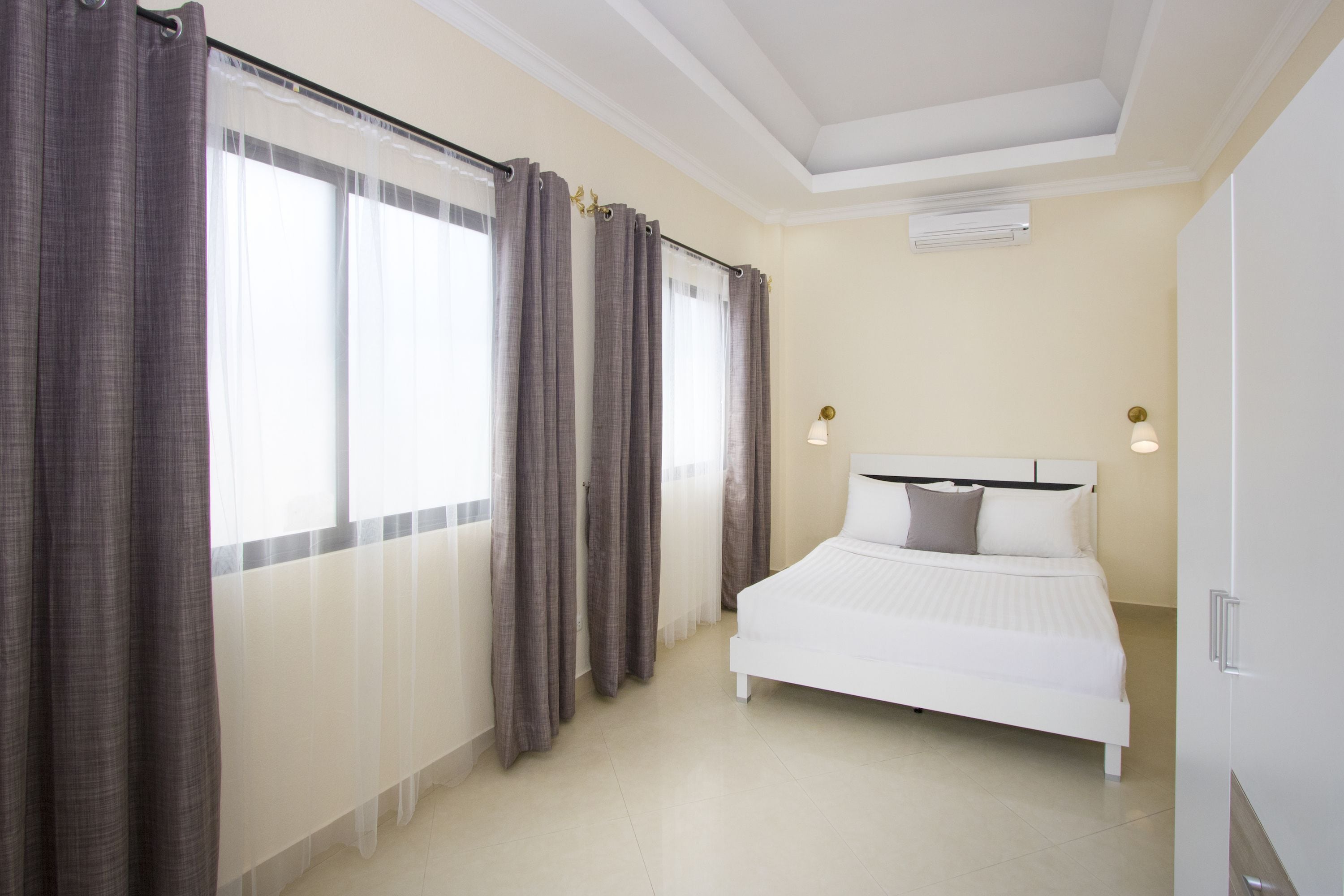 Une chambre à coucher avec un lit, des rideaux, un luminaire au plafond et un radiateur.
