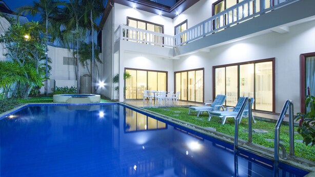 A two-story building with a swimming pool, outdoor seating, and a well-lit balcony. - Avoca Pool Villas (Pattaya)