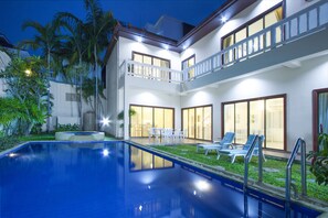 A two-story building with a swimming pool, outdoor seating, and a well-lit balcony. - Avoca Pool Villas (Pattaya)