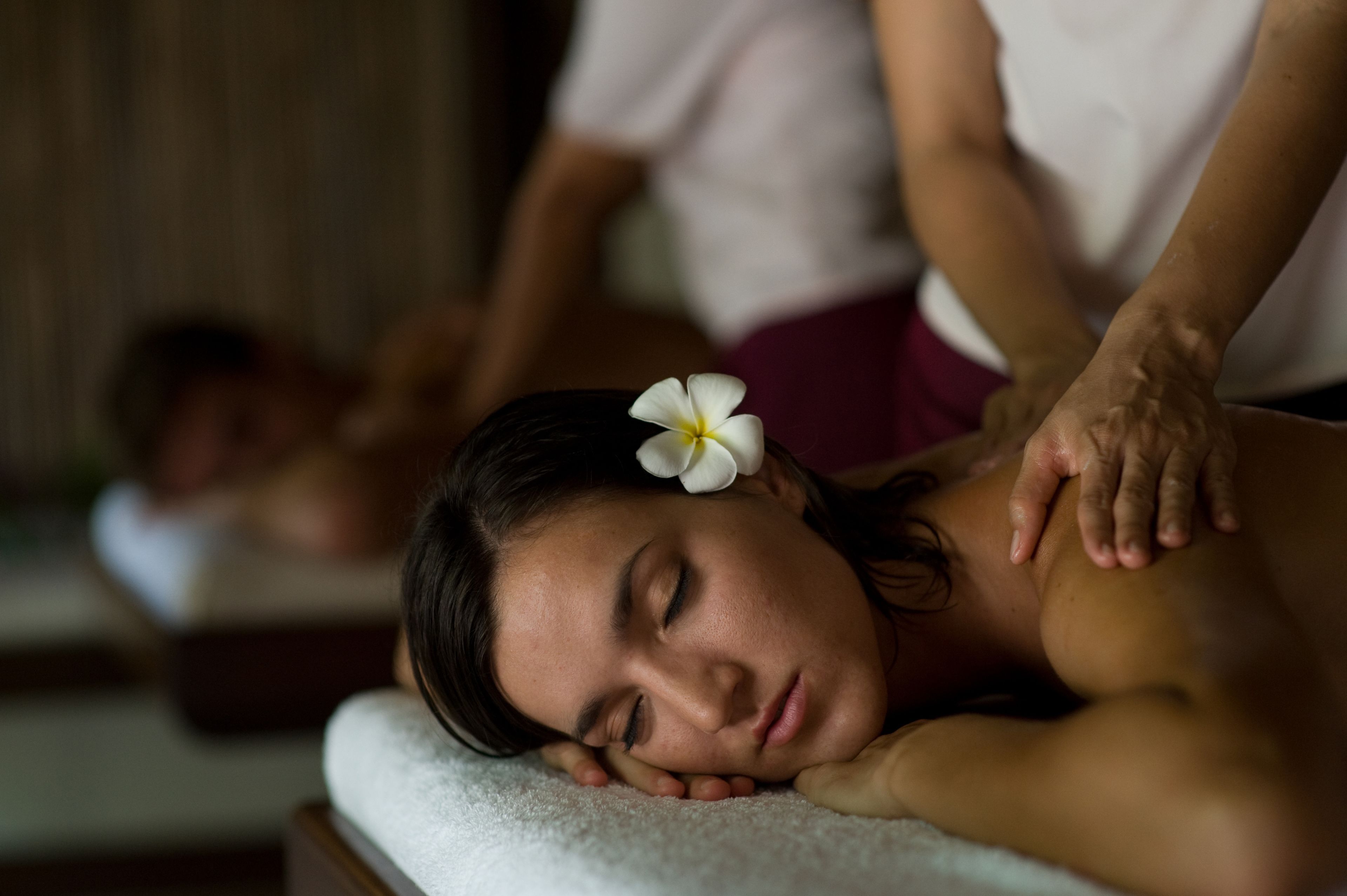 A person receiving a massage in a room with a wooden floor and a white wall.