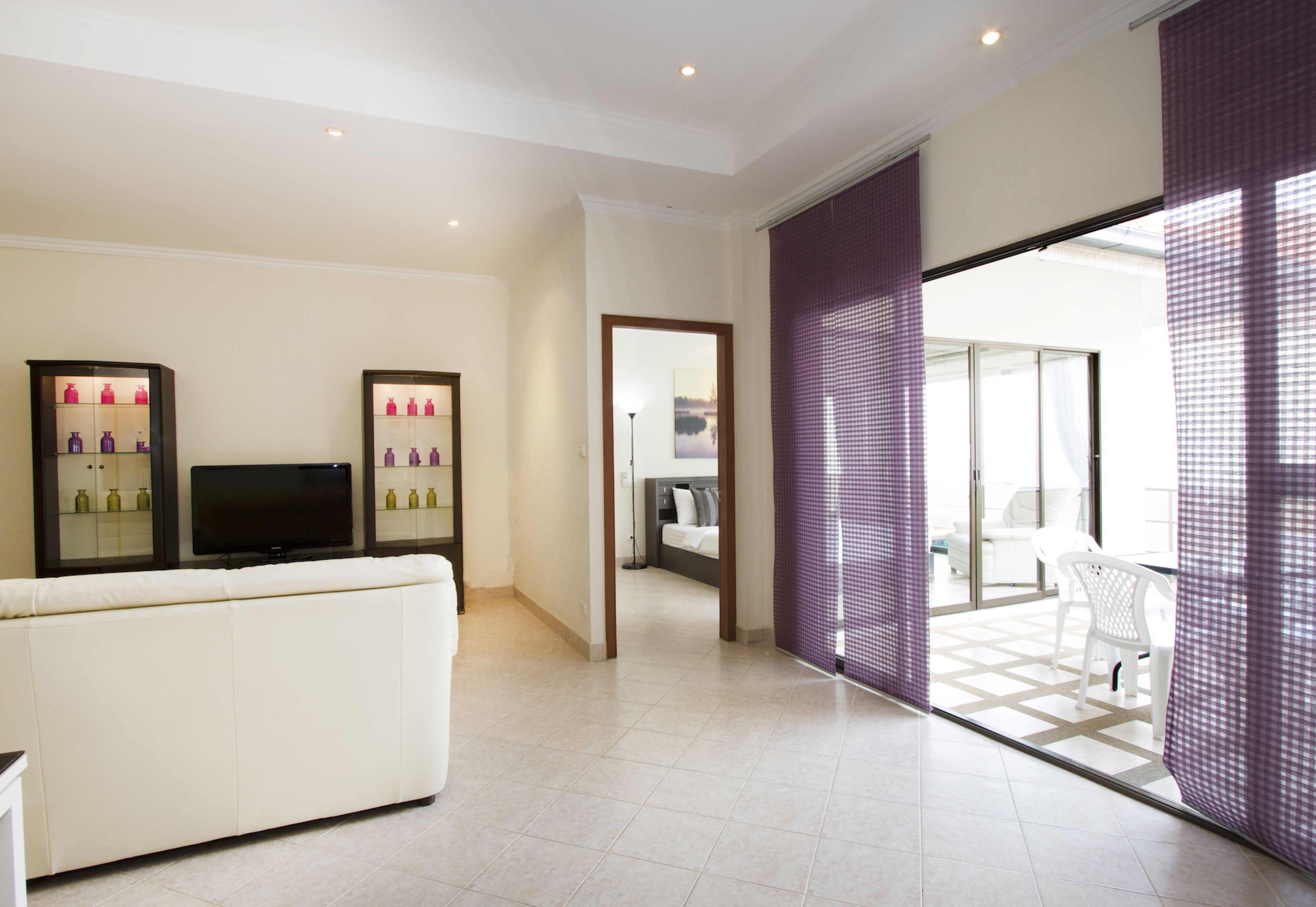 A modern living room with a white sofa, a flat-screen TV, and two glass display cabinets with bottles.