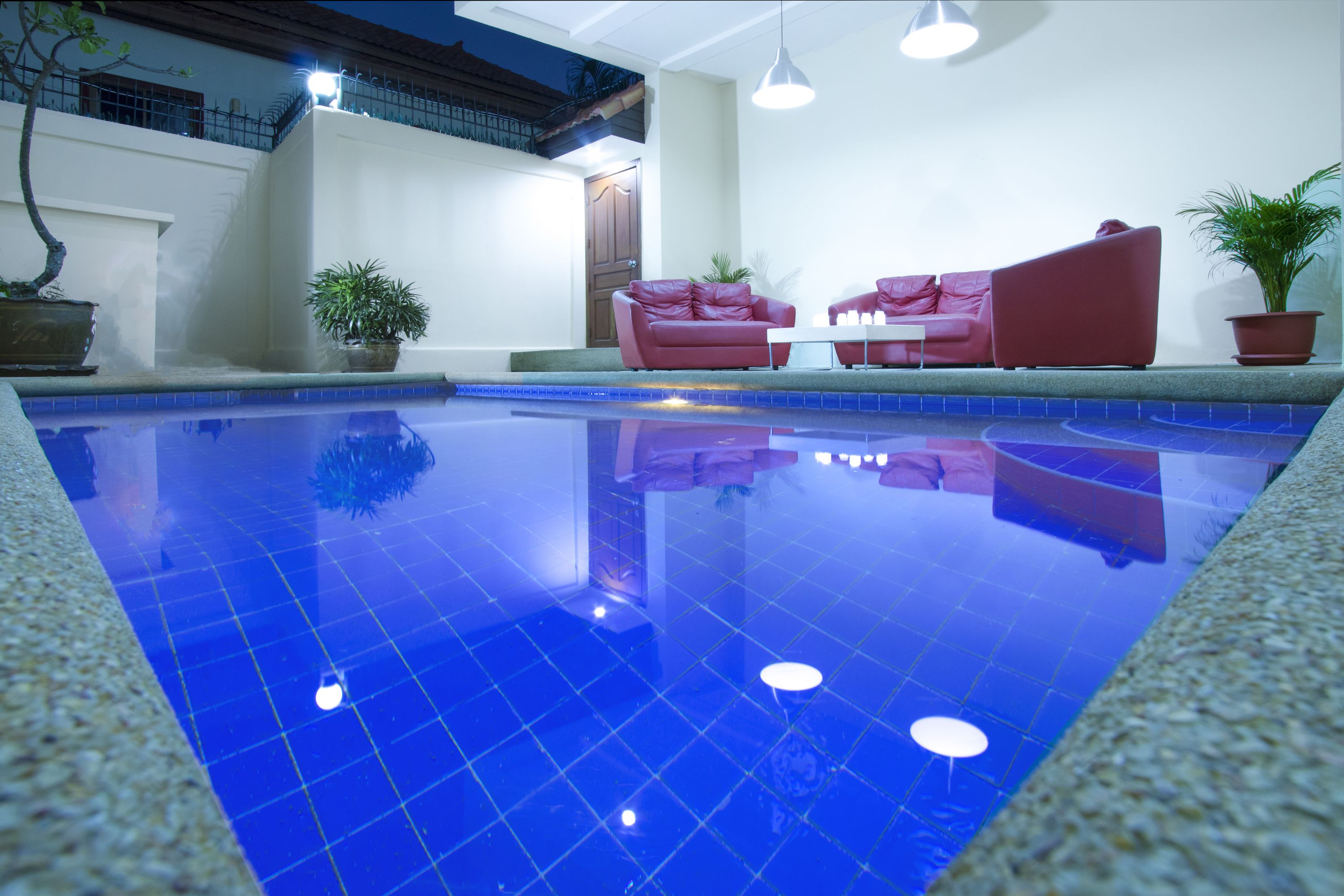 A swimming pool with a tiled floor, surrounded by potted plants and red furniture.