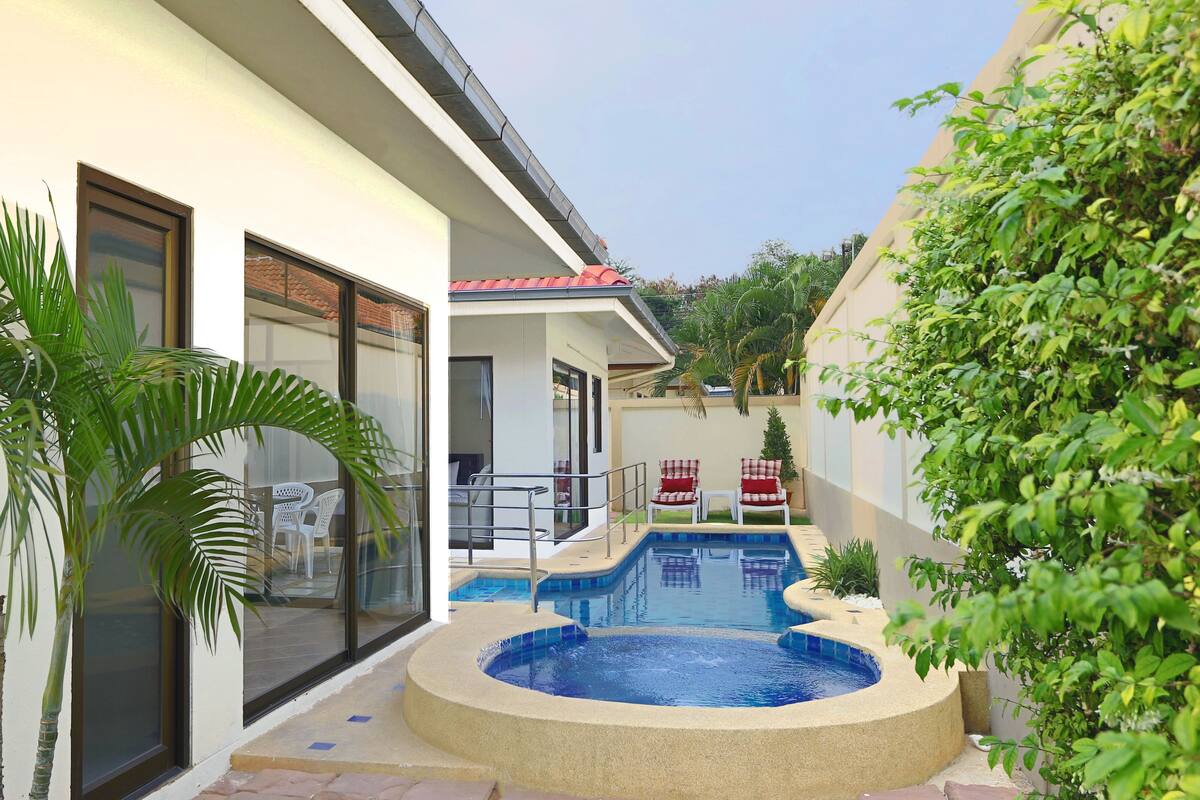 A modern house with a swimming pool, a patio with chairs, and a large window.