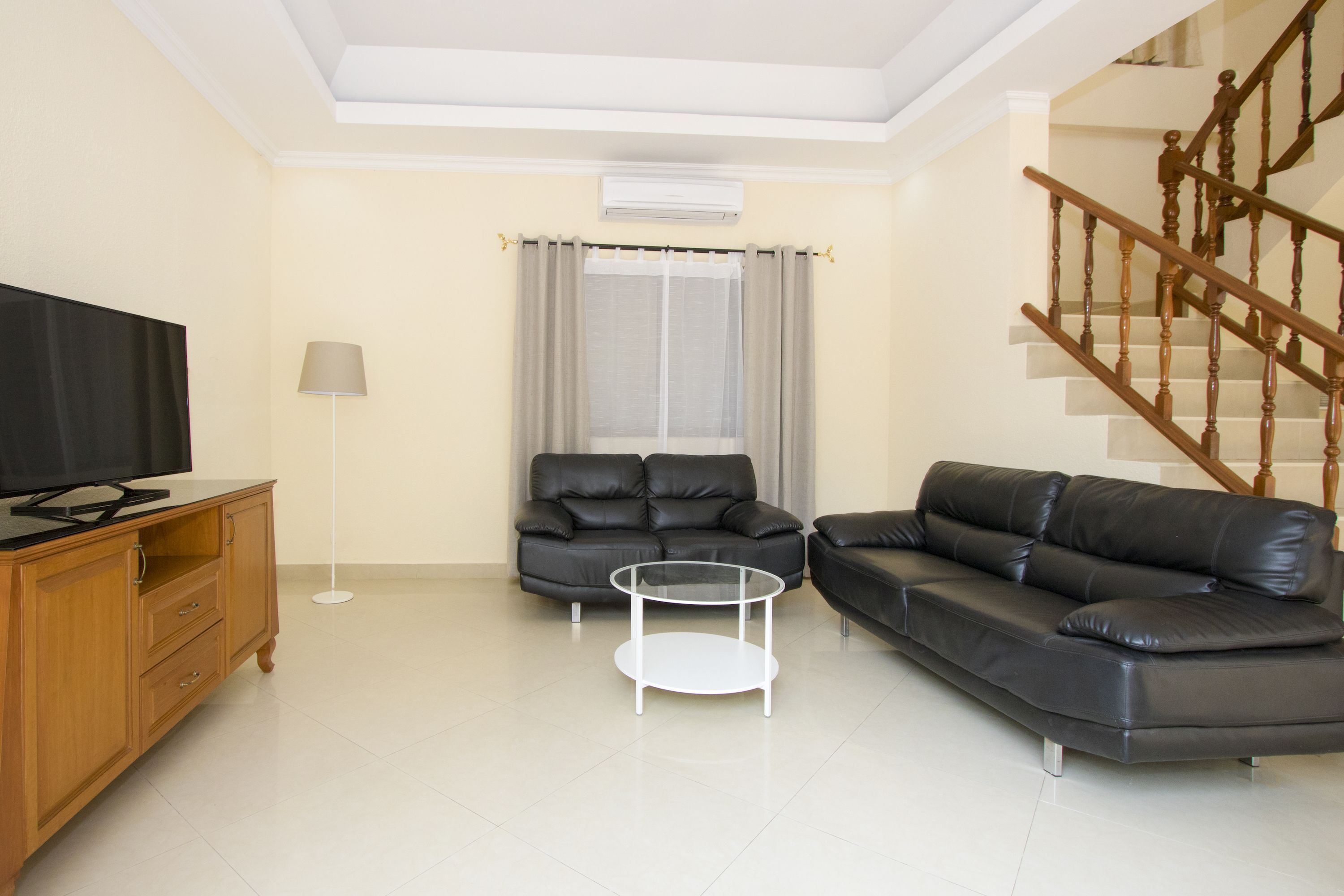 A living room with a sofa, a coffee table, a TV on a wooden cabinet, and a staircase.