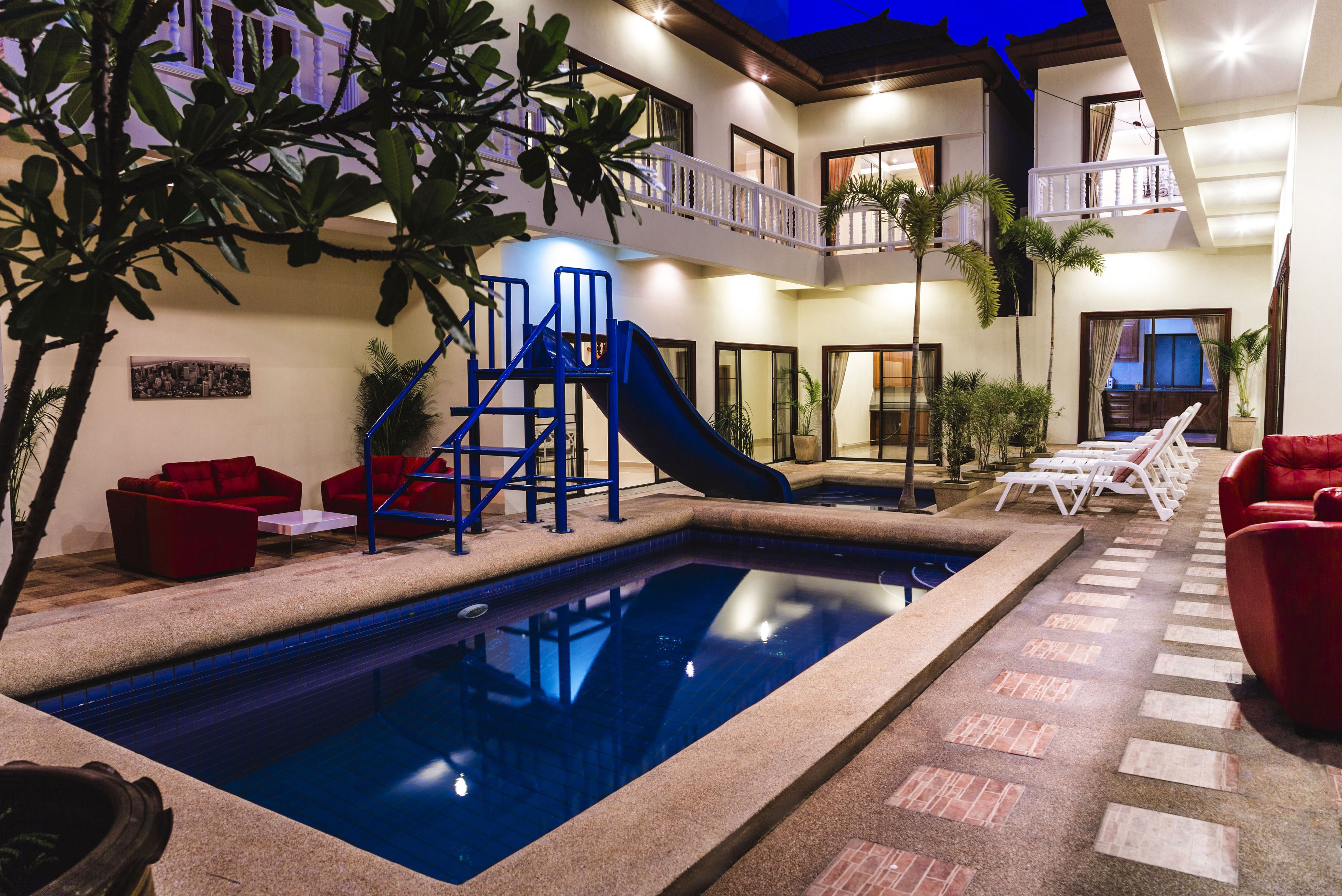 A swimming pool with a slide, red seating, and a balcony with a railing.