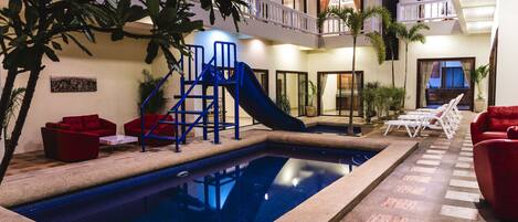 A swimming pool with a slide, red seating, and a balcony with a railing.