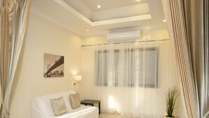A hotel room with a bed, a small table, a potted plant, and a window with sheer curtains. - Avoca Pool Villas (Pattaya)