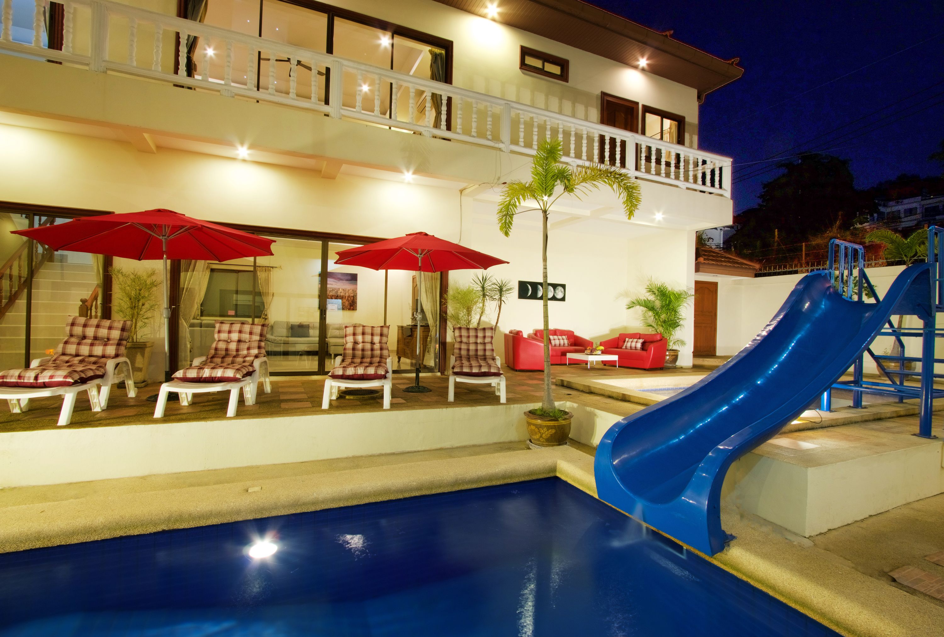 Ein Poolbereich mit Liegestühlen und Sonnenschirmen, eine blaue Rutsche und ein Balkon mit Blick auf den Pool.