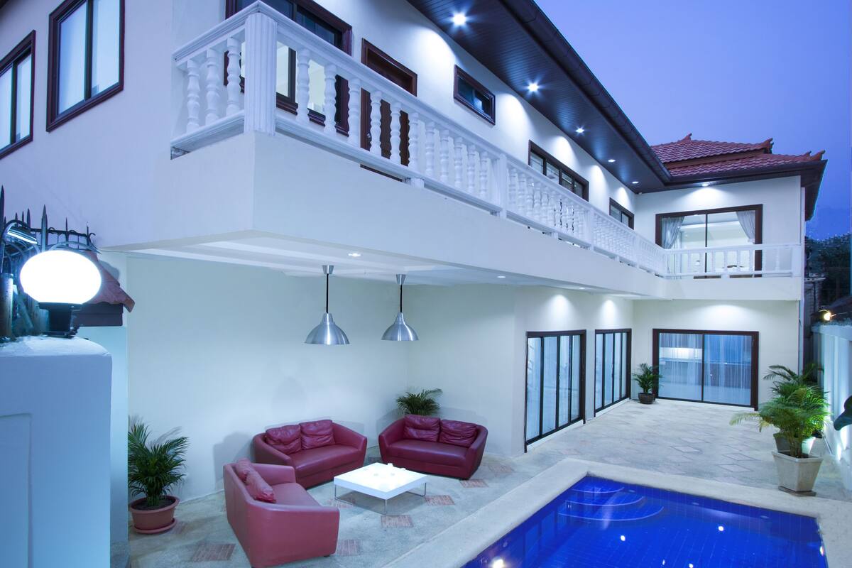 A two-story house with a balcony, a swimming pool, and outdoor seating.