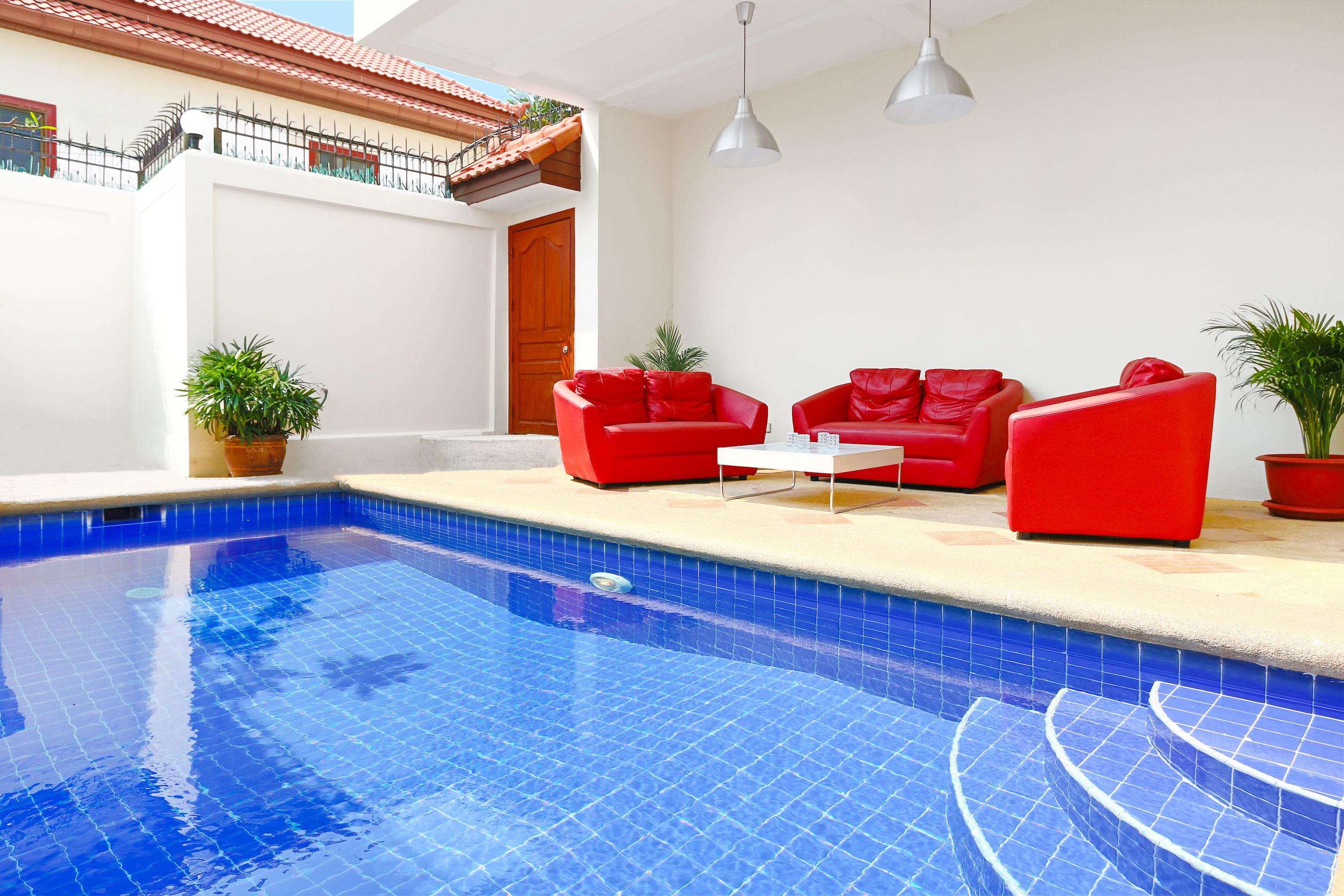 Une piscine avec des canapés rouges et des plantes en pot.