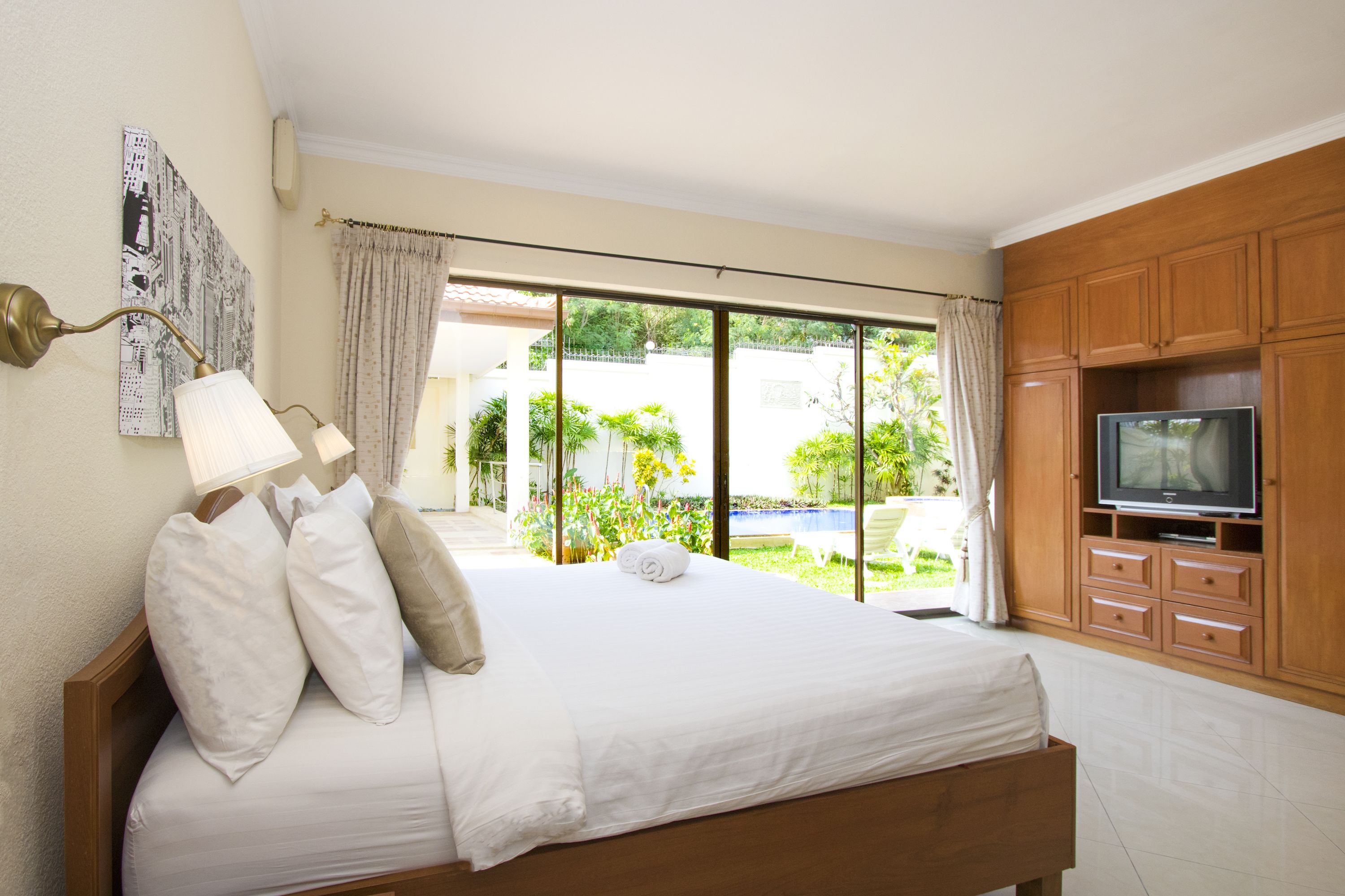Une chambre avec un lit, une télévision et une vue sur une piscine et un espace verdoyant.