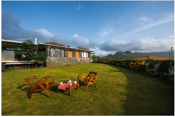 A house with a stone facade, a red-tiled roof, and a grassy lawn with two wooden chairs and a table. - Amanzi - The Boutique Resort (Mawal)