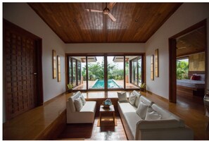 A spacious living room with a wooden ceiling, large windows, and a pool view. - Amanzi - The Boutique Resort (Mawal)