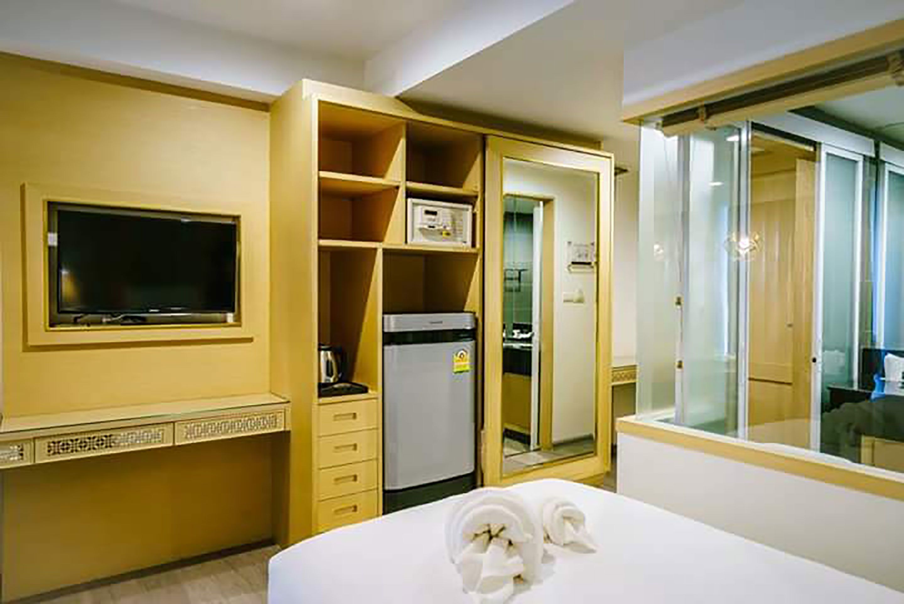 A hotel room with a bed, a television, a minibar, a refrigerator, and a glass-enclosed bathroom.