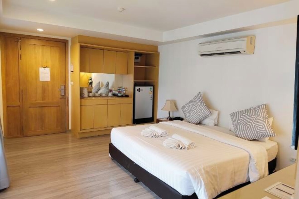 Habitación de hotel con cama, escritorio, armario, mini refrigerador y aire acondicionado.