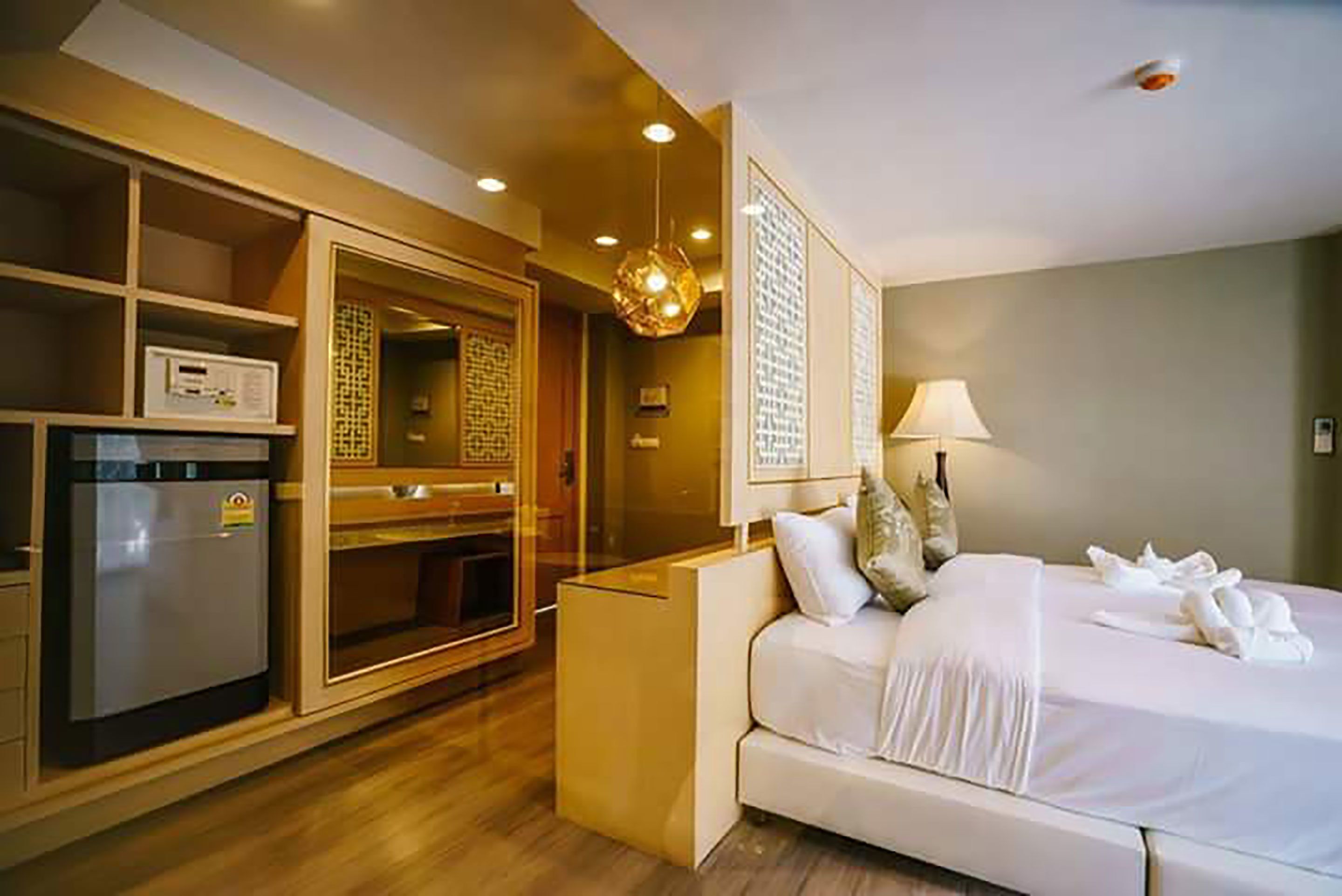 Una habitación de hotel con cama, escritorio con computadora, armario e iluminación colgante.