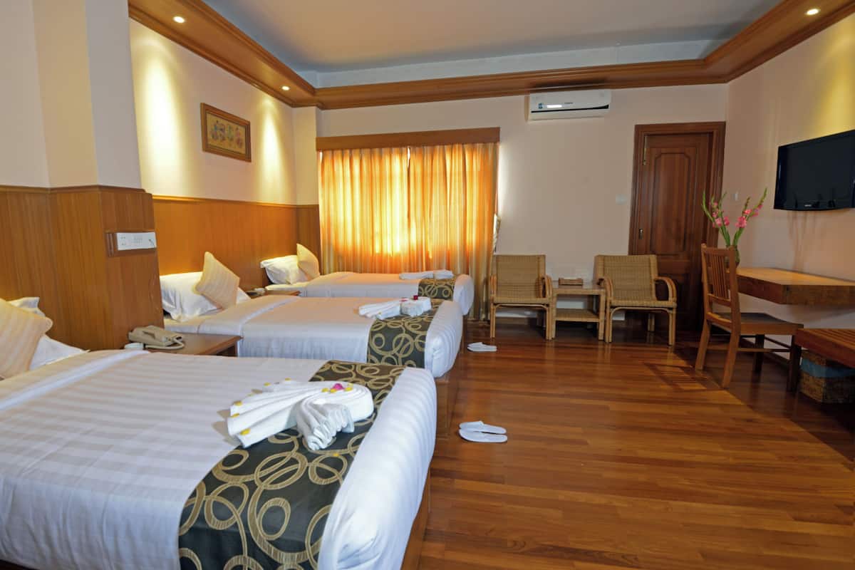 A hotel room with four beds, a wooden floor, a TV, and a desk with chairs.
