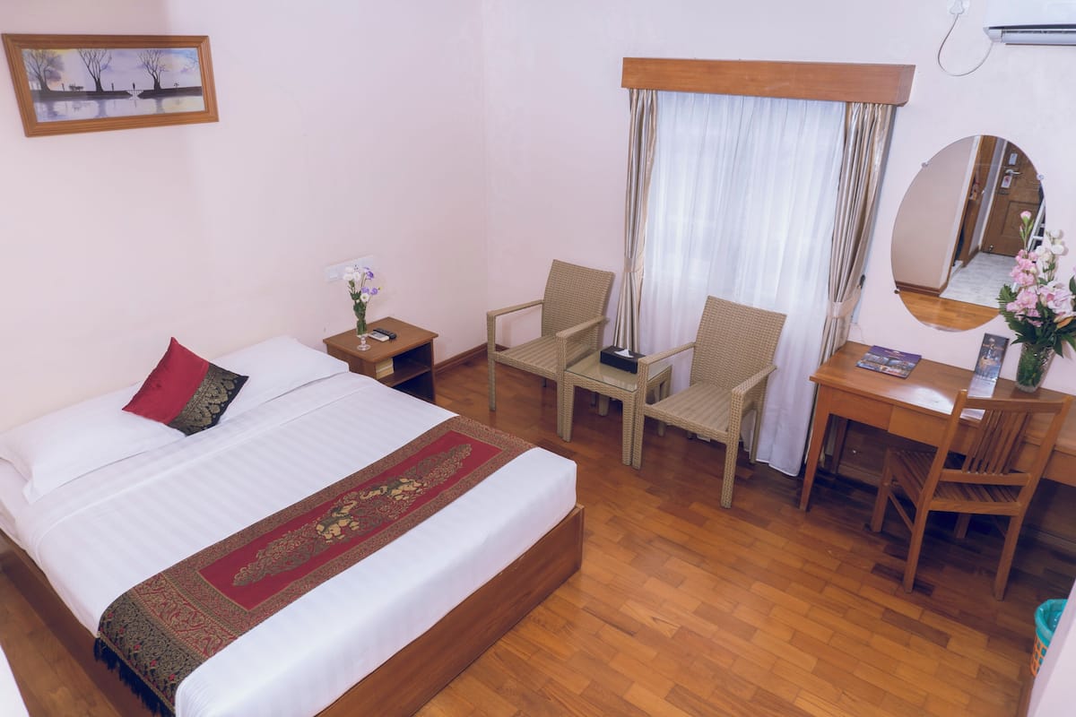 A bedroom with a bed, two chairs, a desk, and a mirror.