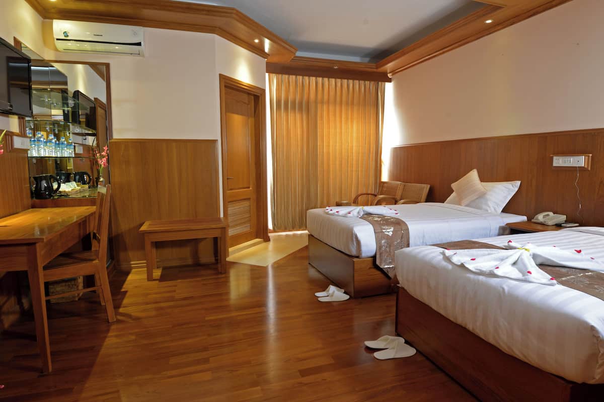 A hotel room with two beds, a desk, a chair, and a TV.