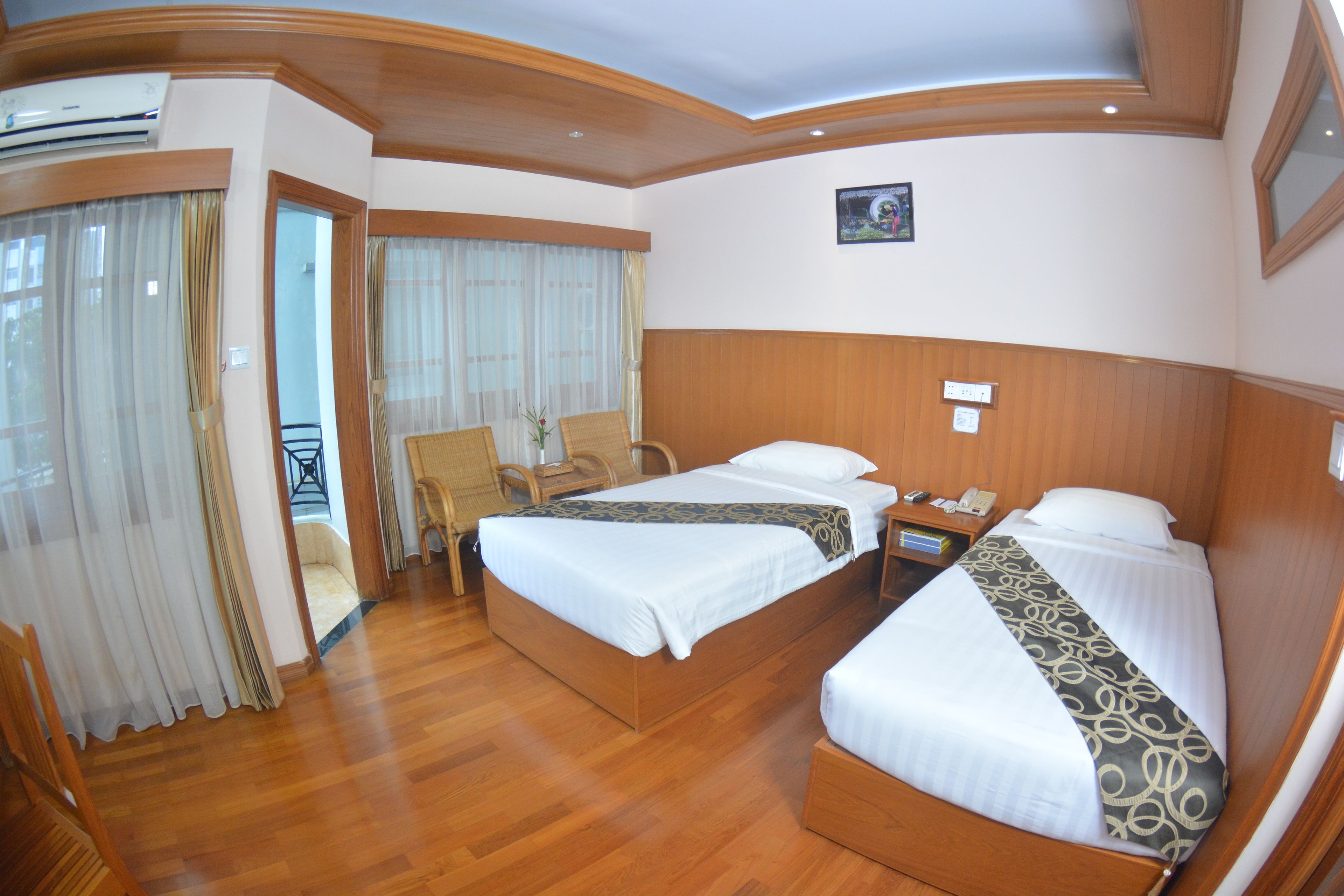 A hotel room with two beds, wooden flooring, a small table, and a chair.