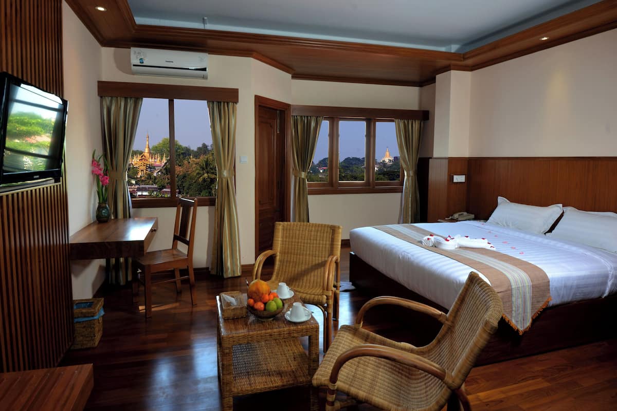 A hotel room with a bed, a desk, a chair, a television, and a view of a temple through the windows.