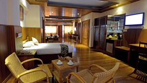 Ein Hotelzimmer mit einem Bett, einem Schreibtisch mit Telefon, Korbstühlen, einem kleinen Tisch mit Tassen und einem Fernseher an der Wand.