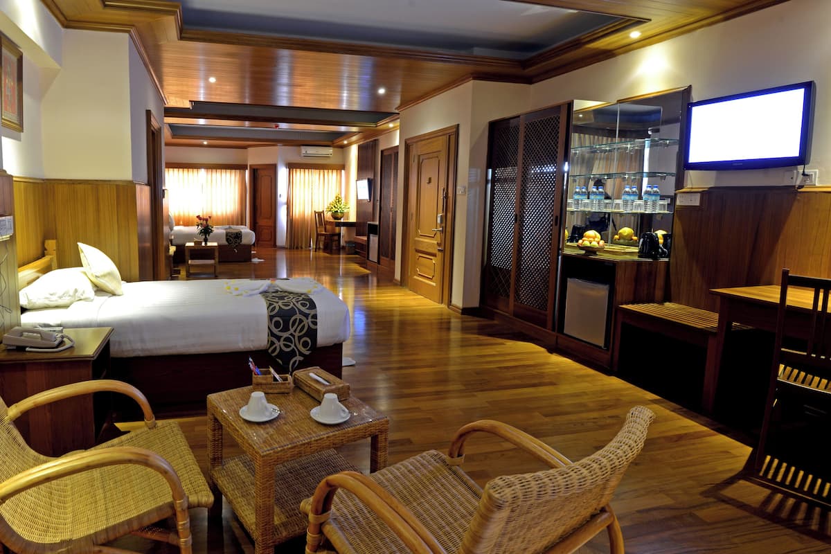 A hotel room with a bed, a desk with a telephone, wicker chairs, a small table with cups, and a television on the wall.