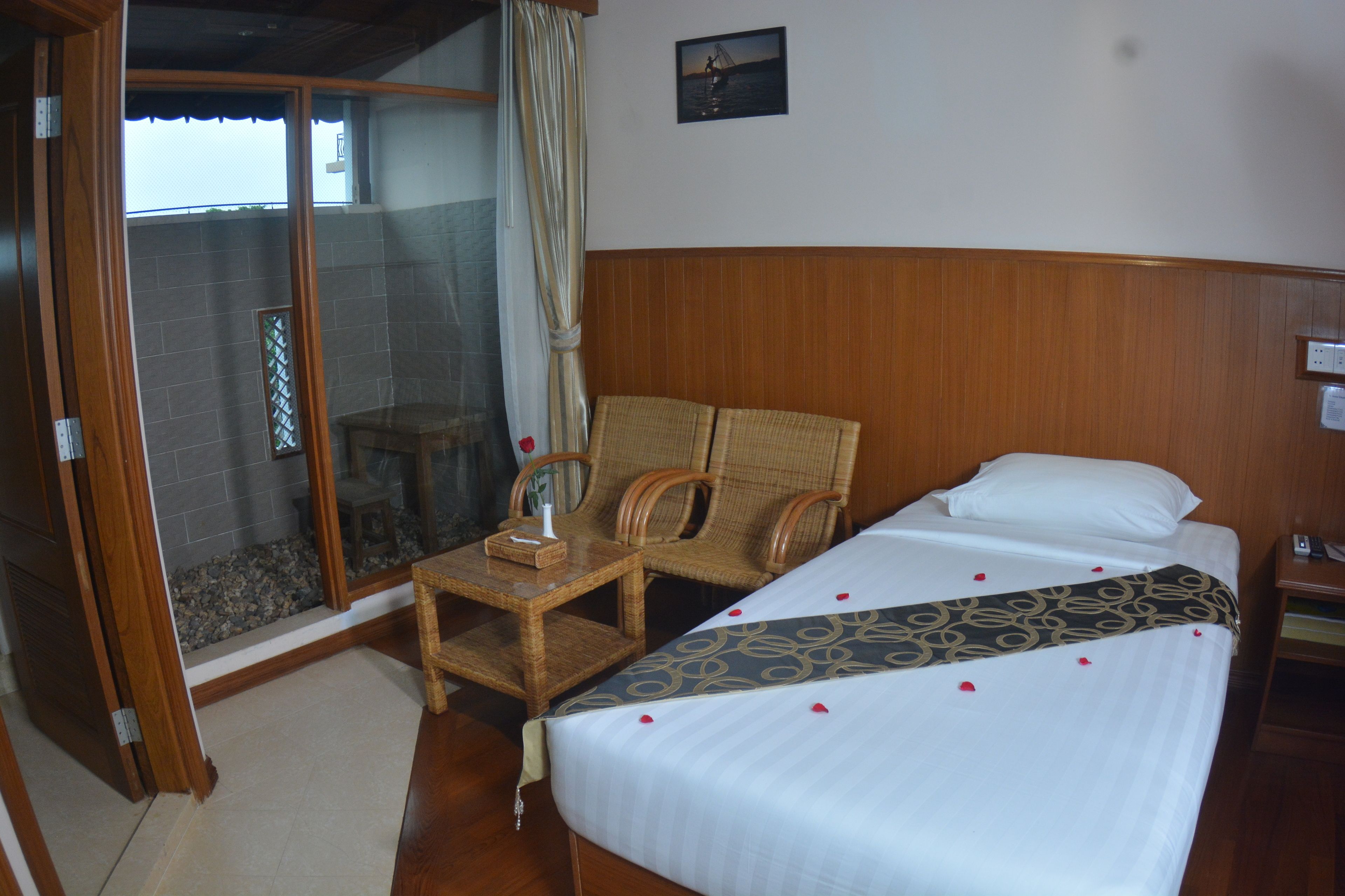 A hotel room with a bed, two wicker chairs, a small table, and a view of the sea through a glass door.