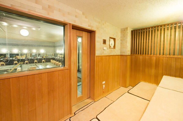 Habitación de hotel con suelo de madera, un espejo grande, una puerta de madera y un reloj en la pared.