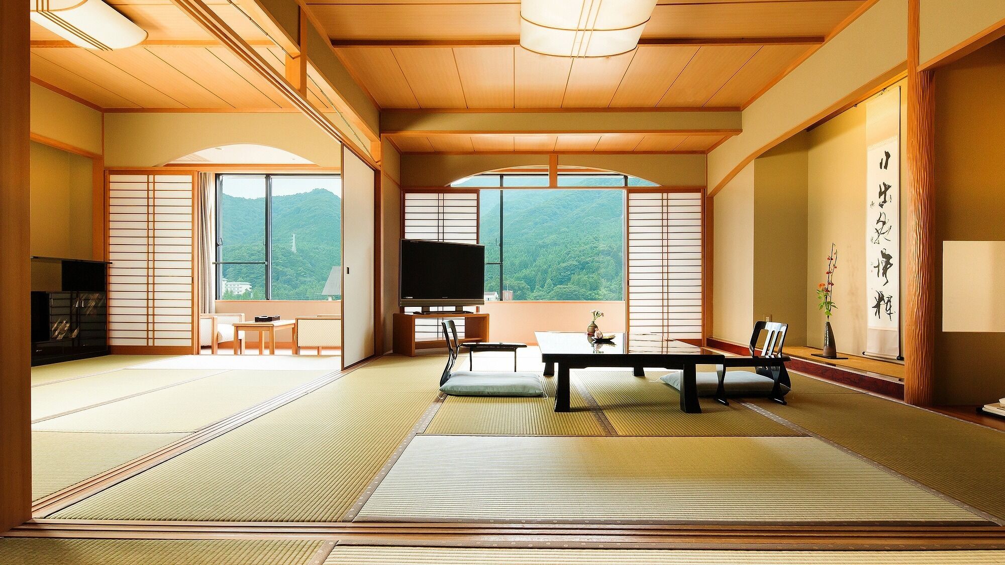 Ein traditioneller japanischer Raum mit Tatami-Boden, einem Fernseher, einem Tisch und Blick auf einen Berg.