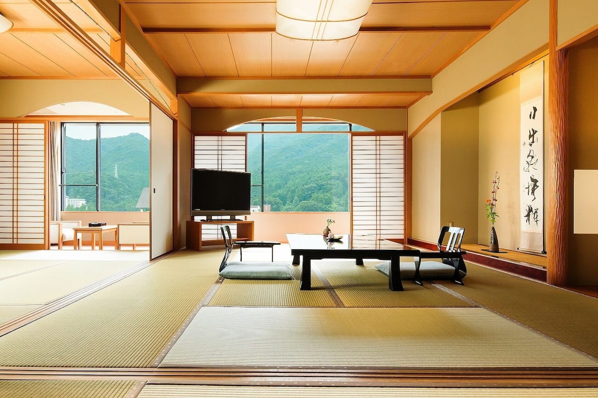 A traditional Japanese room with tatami flooring, a television, a table, and a view of a mountain.