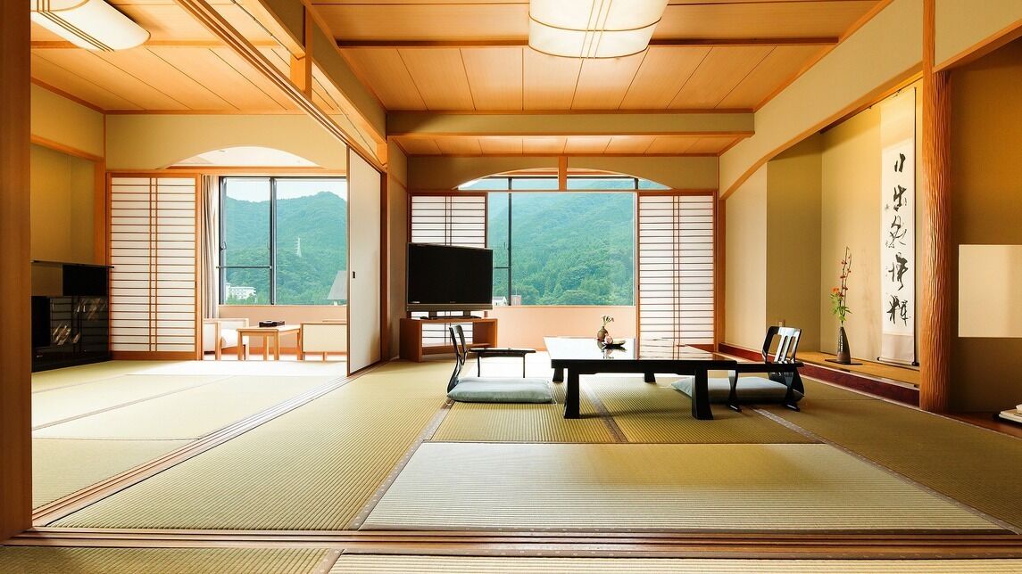 Ein traditioneller japanischer Raum mit Tatami-Boden, einem Fernseher, einem Tisch mit Stühlen und Blick auf die Berge.