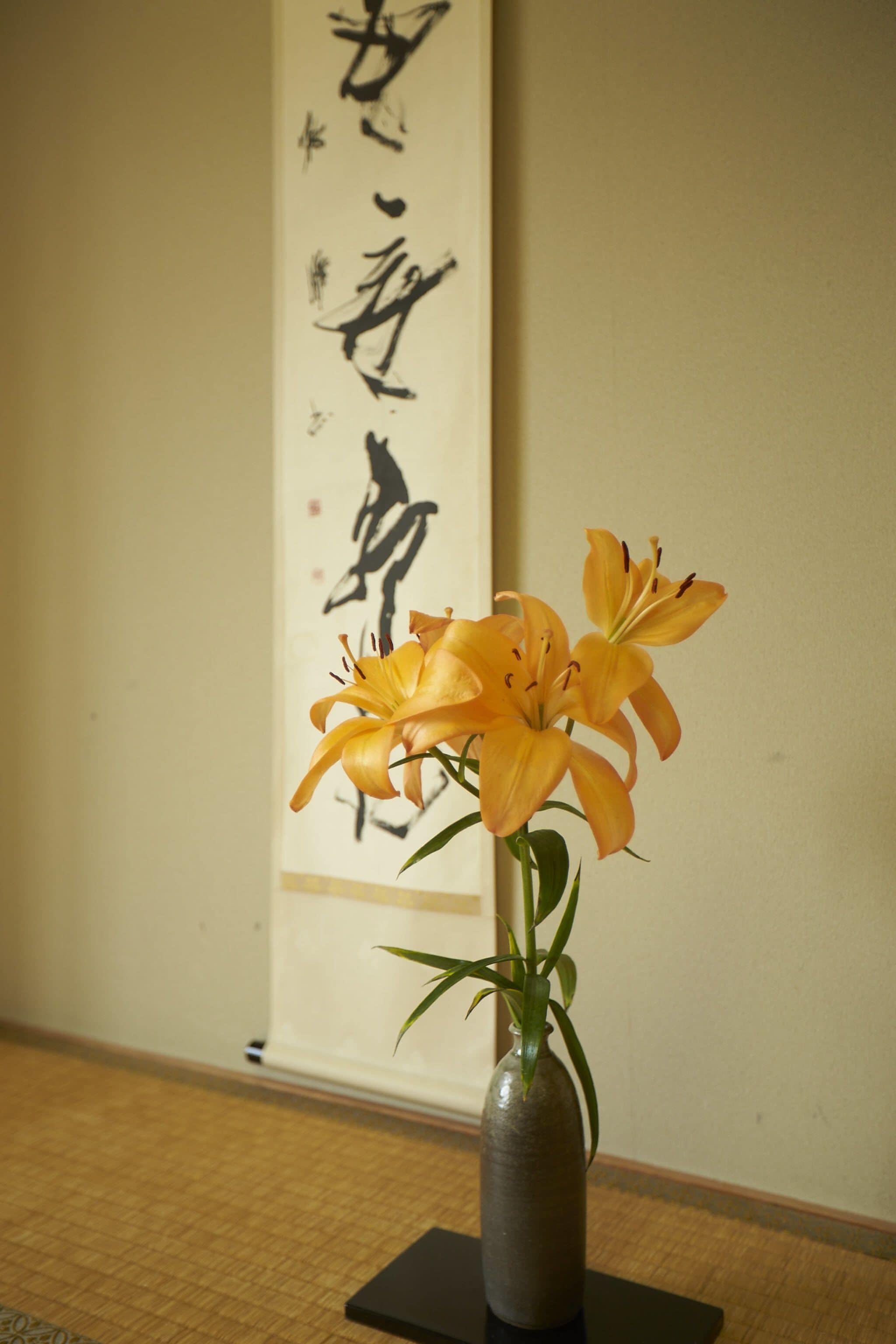 A vase with flowers on a table in a room with a wall featuring calligraphy.