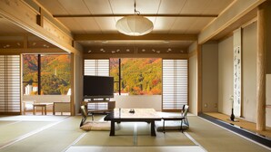 A traditional Japanese room with tatami flooring, a tatami mat table, a television, and a view of autumn foliage through large windows. - Kinugawa Onsen Sanraku (Nikko)