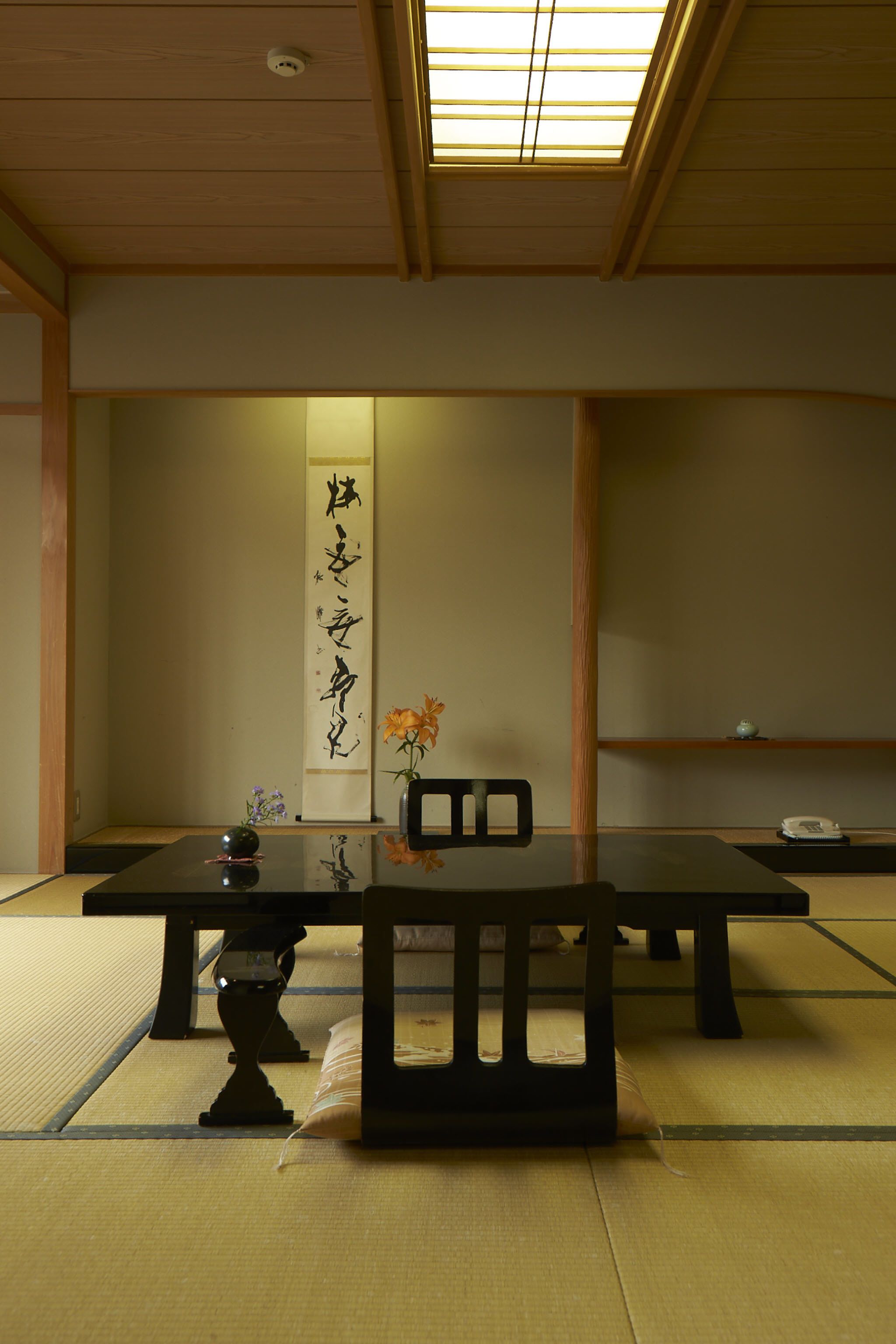 A traditional Japanese room with tatami flooring, a low table, a chair, and a calligraphy scroll on the wall.