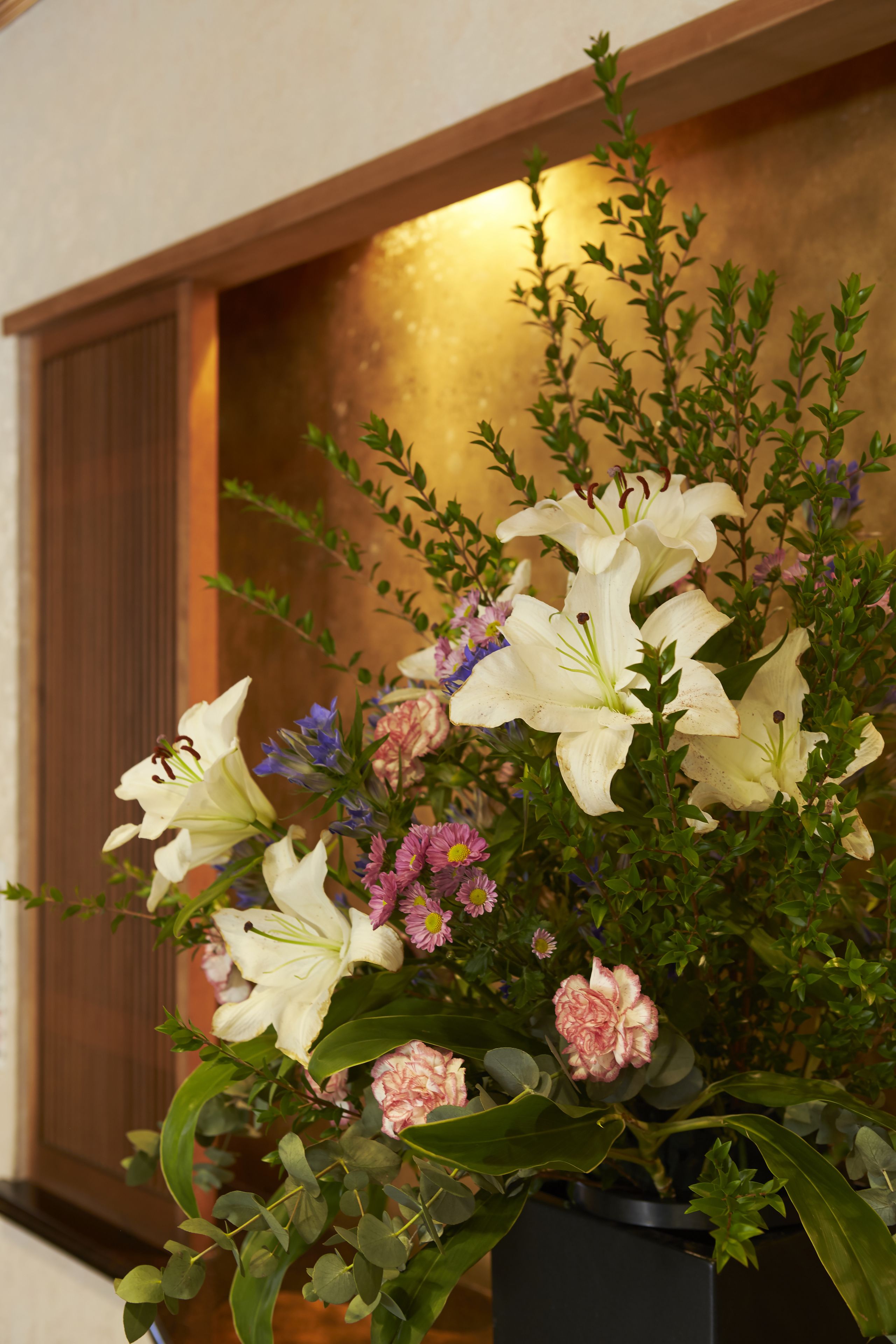A potted floral arrangement with white lilies, pink carnations, and purple flowers.