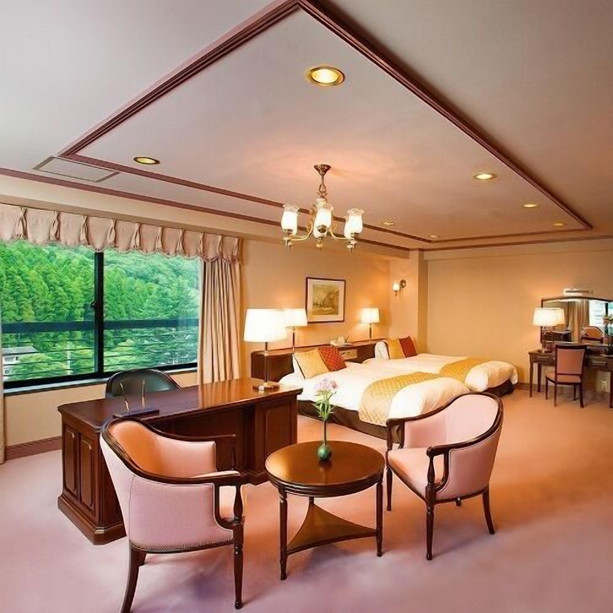 Ein Hotelzimmer mit einem großen Bett, einem Schreibtisch, zwei Stühlen, einem kleinen Tisch und Blick auf Grünflächen.