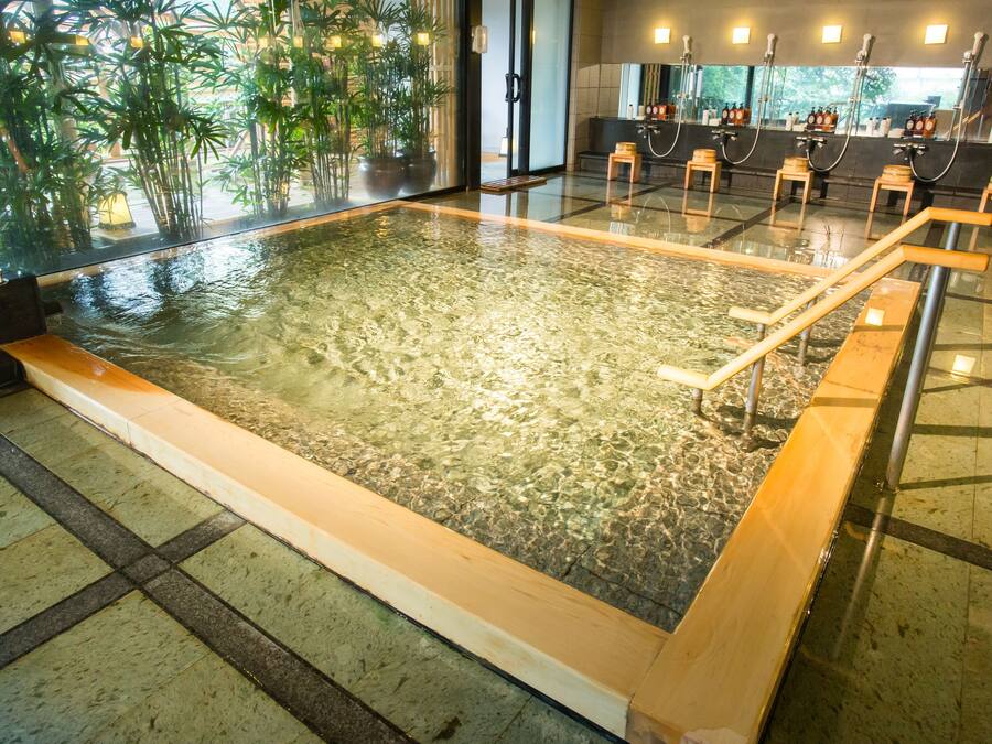 Una amplia piscina interior con agua cristalina, rodeada de suelo de baldosas y bancos de madera.