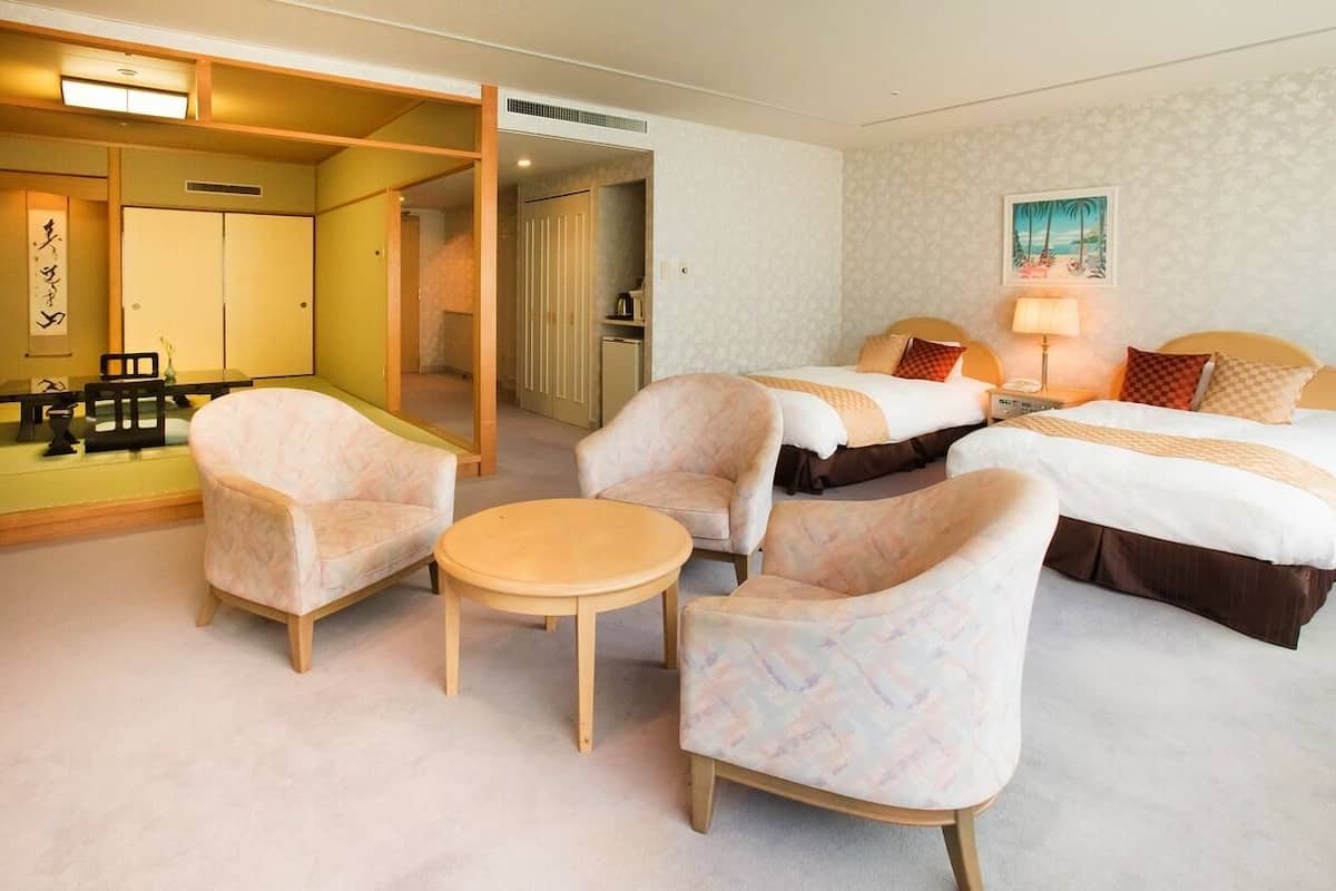 Une chambre d’hôtel avec deux lits, une petite table, deux fauteuils, un miroir et un tableau au mur.