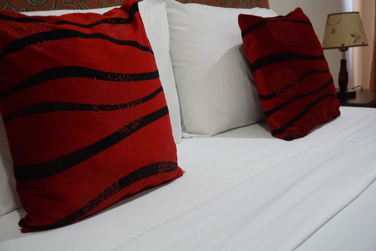 A bed with white sheets and two red pillows with black stripes.