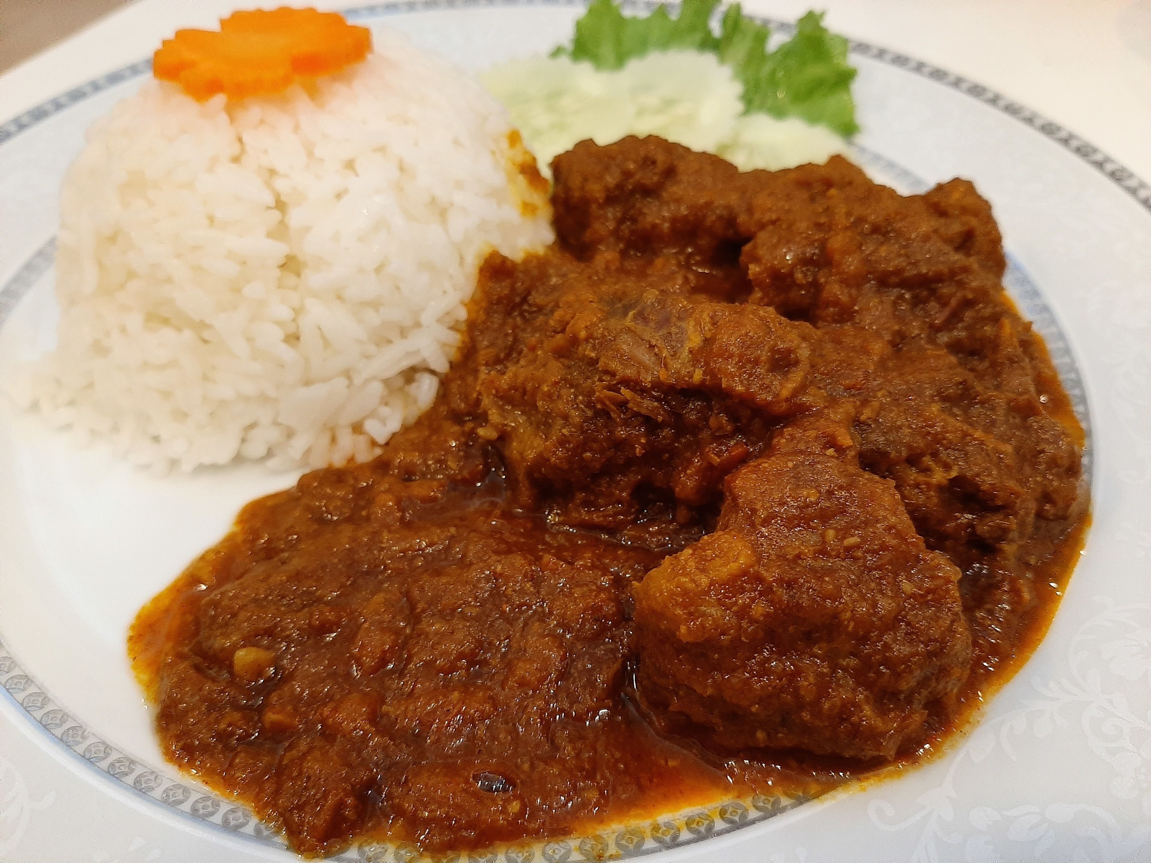 Un plato con arroz blanco, un guiso de carne y verduras acompañantes.