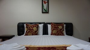 A neatly made bed with a red and gold patterned bedspread, two white pillows, and a single red and green framed picture on the wall. - Phounsiri Hotel (Ban Donnoun)