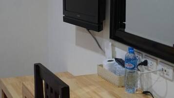 A small room with a wooden desk, a chair, a television mounted on the wall, and a water bottle on the desk.