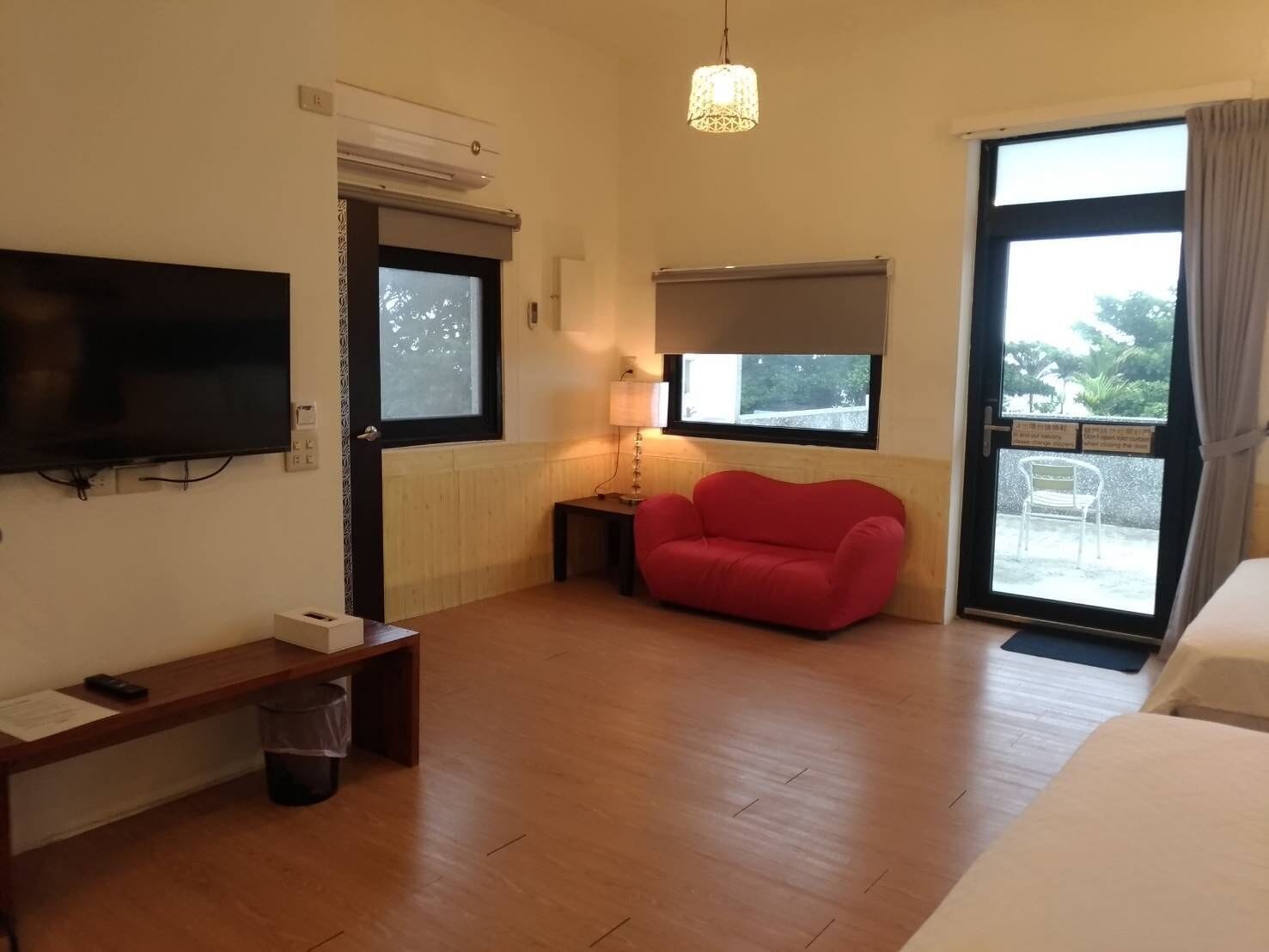 A room with a television, a red sofa, a small table, and a bench.