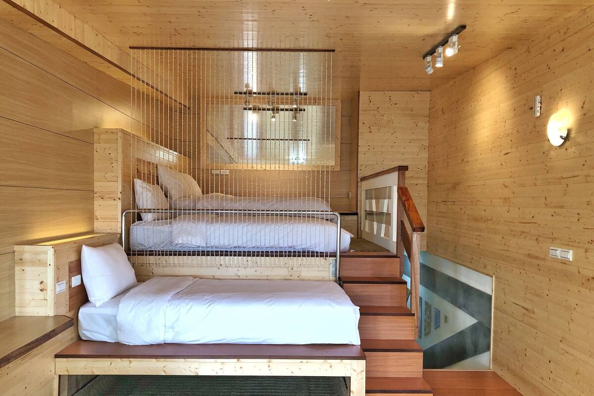 A wooden cabin room with a bunk bed, a small desk, and a staircase.